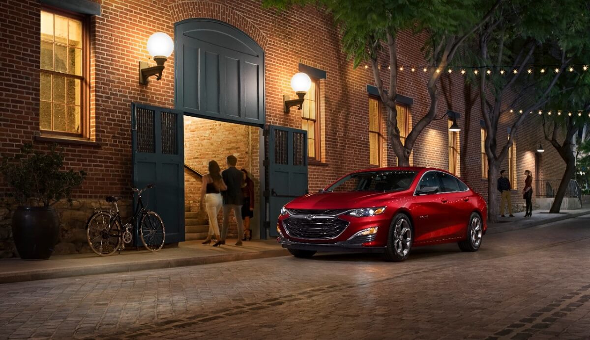 A red 2020 Chevrolet Malibu parks next to a restaurant.