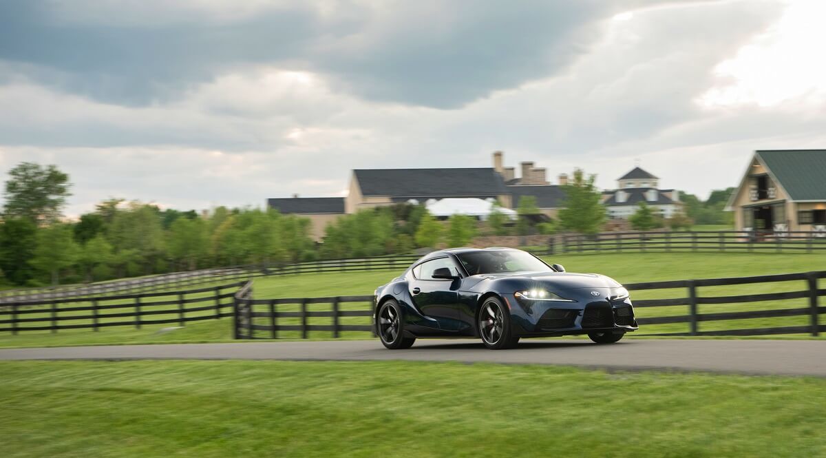 A blue 2020 Toyota GR Supra drives past a horse farm. 