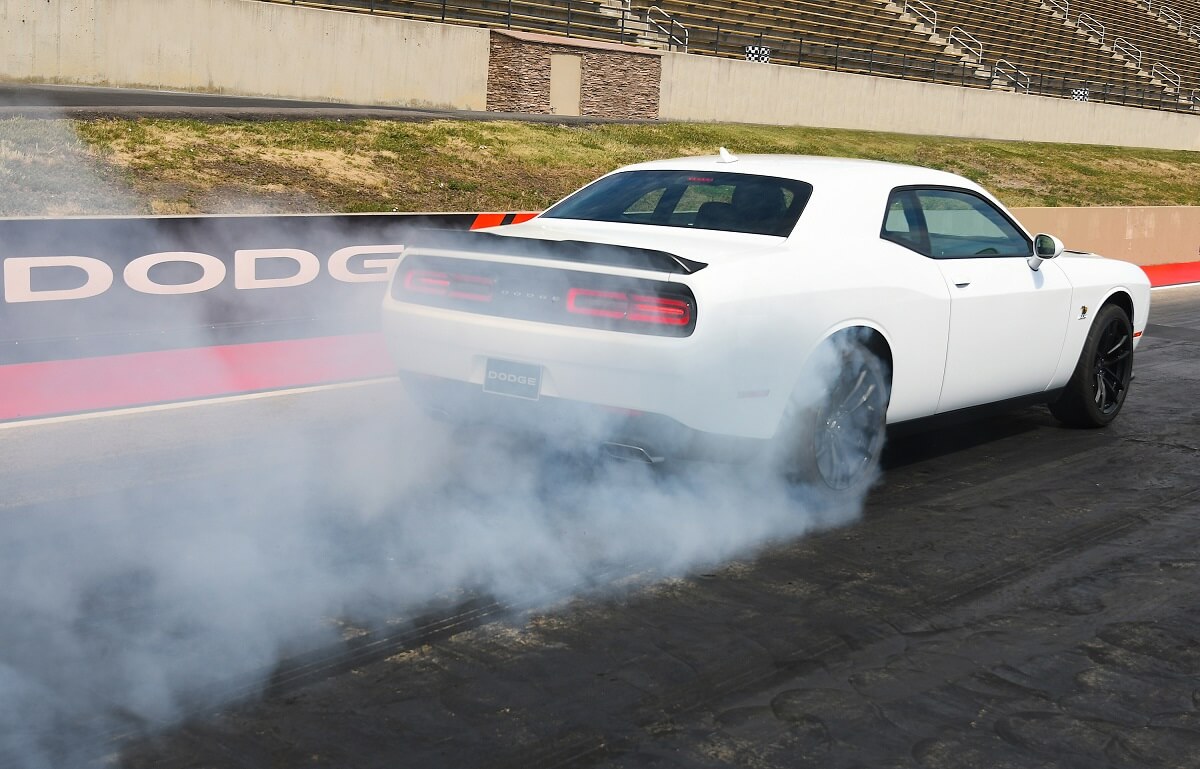 A white Dodge Challenger R/T lights up its tires during a burnout at a drag strip.