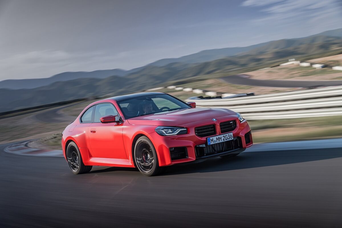 An orange 2023 BMW M2 takes a corner on a closed track.