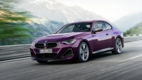 A purple BMW M240i xDrive cruises by a mountain range.