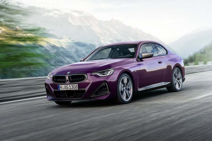 A purple BMW M240i xDrive cruises by a mountain range.