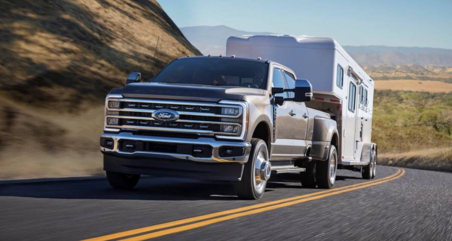 A 2023 Ford Super Duty F-350 Lariat heavy-duty pickup truck model towing a trailer up a country highway hill