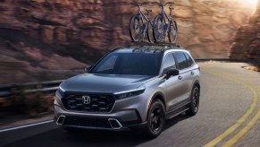 A gray 2023 Honda CR-V Hybrid small hybrid SUV is driving on the road.