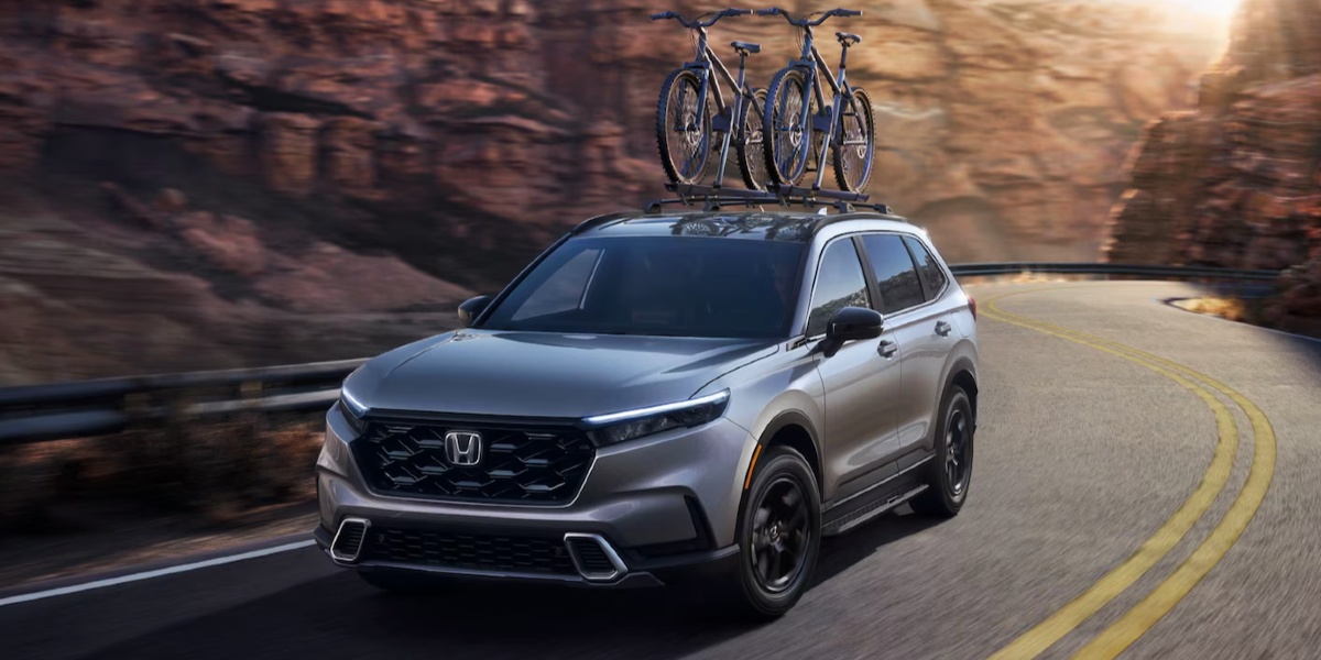 A gray 2023 Honda CR-V Hybrid small hybrid SUV is driving on the road.