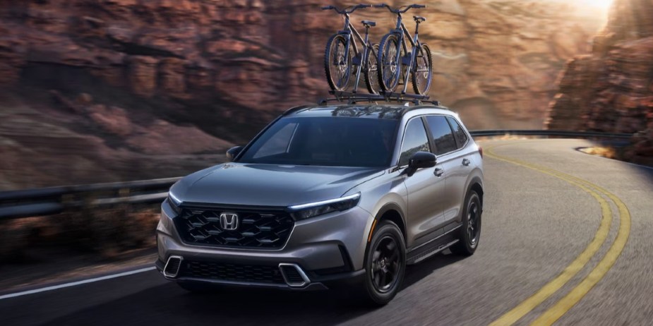 A gray 2023 Honda CR-V Hybrid small hybrid SUV is driving on the road. 