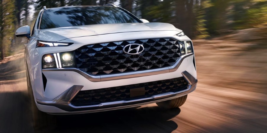 A white 2023 Hyundai Santa Fe midsize SUV is driving off-road.