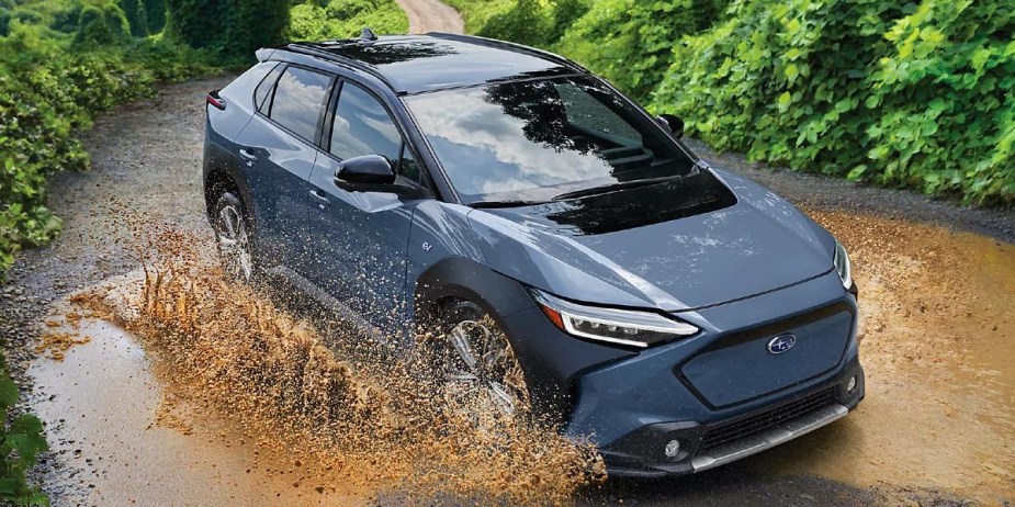 A blue 2023 Subaru Solterra is driving through the mud. 