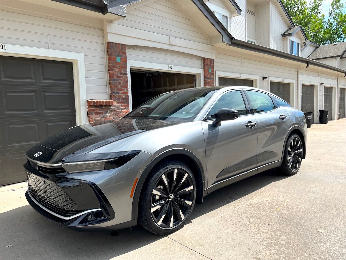 A front corner view of a 2023 Toyota Crown in front of garages