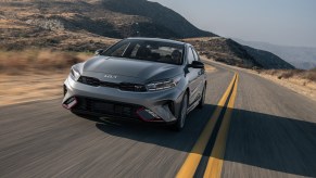 A manual transmission grey 2023 Kia Forte GT driving down the road in the mountains with red accents