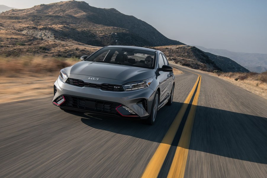 A manual transmission grey 2023 Kia Forte GT driving down the road in the mountains with red accents