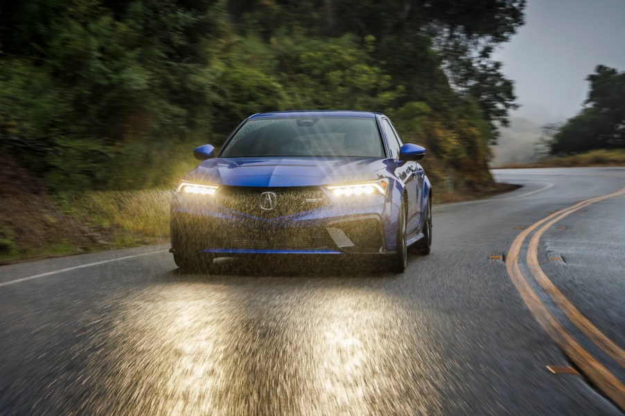 A blue 2024 Acura Integra trim (Type S) driving in the rain on a winding road.