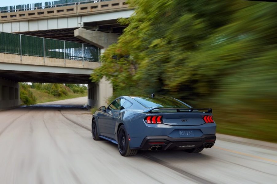 A blue 2024 Ford Mustang GT drives down a park road.