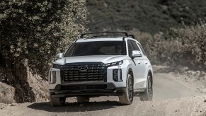 The white 2024 Hyundai Palisade on a dusty road. The Hyundai Palisade sales figures lag behind other Hyundai SUVs