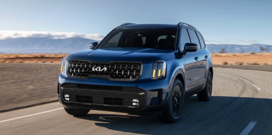 A blue 2024 Kia Telluride midsize three-row SUV is driving on the road. 