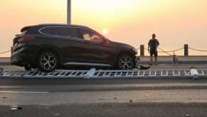 A BMW X3 luxury SUV sits on a safety barrier after a crash.