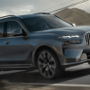 A 2024 BMW X7 full-size luxury SUV model driving down a country highway past phone lines