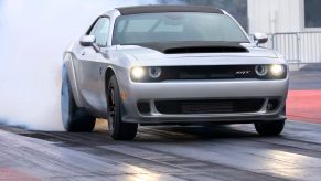 A silver and black Dodge Challenger SRT Demon 170 does a burnout on a drag strip.