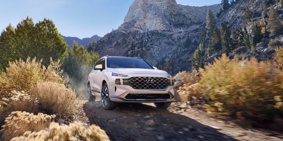 A white 2023 Hyundai Santa Fe midsize SUV is driving off-road. 