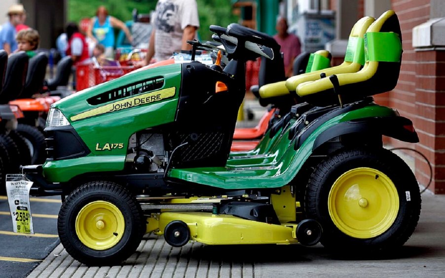 A lineup of yellow and green John Deere riding mowers sit on a platform.