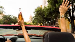 A convertible passenger holding an open container of alcohol above their head.