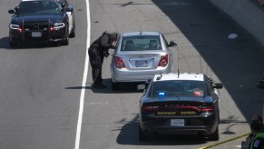 A silver compact car was the victim of a road rage incident in California. Two police cars stay nearby to keep things safe.