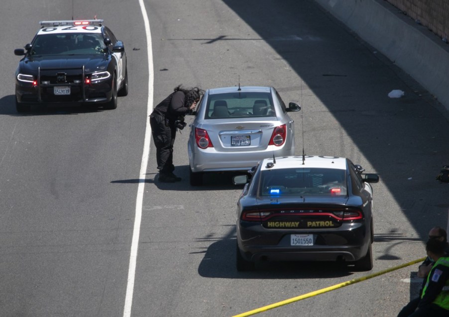 A silver compact car was the victim of a road rage incident in California. Two police cars stay nearby to keep things safe.