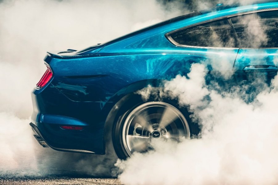 A bright blue S550 Ford Mustang roasts its tires in typical muscle car fashion.