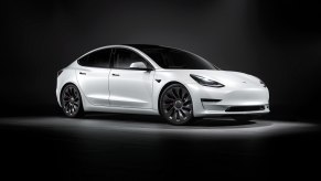 A white 2023 Tesla Model 3 parks under overhead lighting on a stage