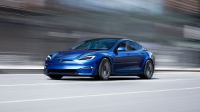 A blue Tesla Model S cruises on a city street.