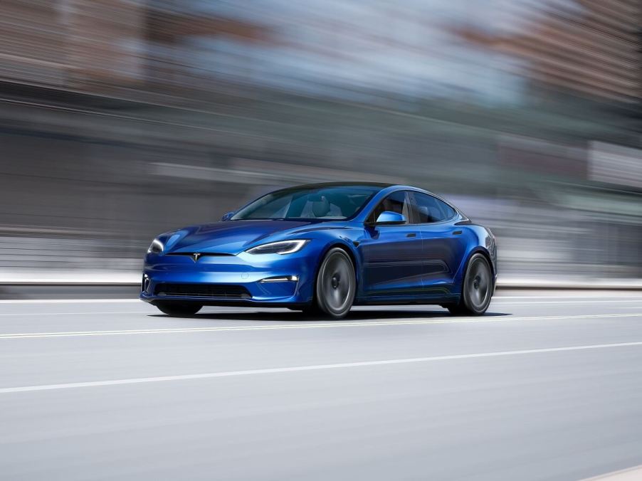 A blue Tesla Model S cruises on a city street.