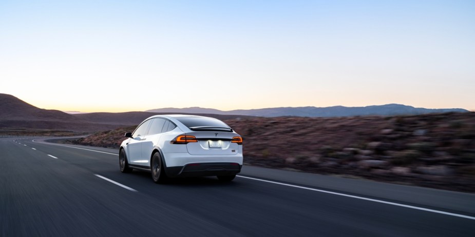 A white 2023 Tesla Model X is driving down the road. 