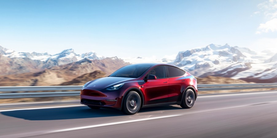 A red 2023 Tesla Model Y small electric SUV is driving on the road.