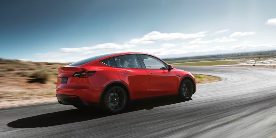 A red 2023 Tesla Model Y small electric SUV is driving on the road.