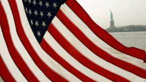 The U.S.A. national flag in the foreground, with the statue of liberty standing in the background.