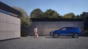 A side profile shot of a 2024 Cadillac XT5 compact luxury SUV model parked on a gravel plaza as a woman walks away