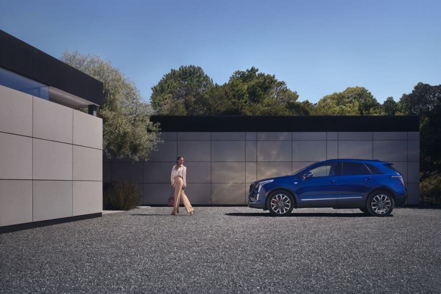 A side profile shot of a 2024 Cadillac XT5 compact luxury SUV model parked on a gravel plaza as a woman walks away