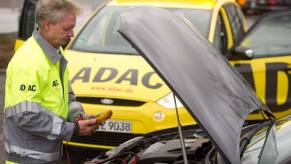 A roadside assistance worker jump starts a car on the side of the road.