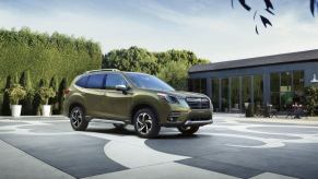 A light-green 2023 Subaru Forester compact SUV model parked on a open plaza surrounded by tall hedges