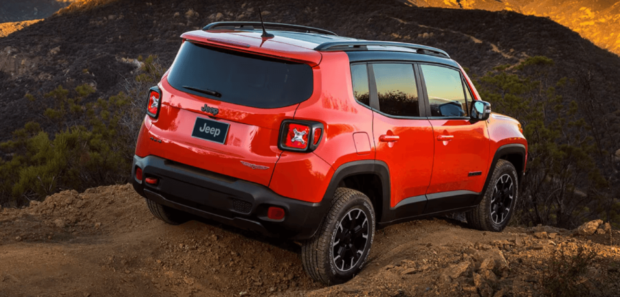 A rear shot of a 2023 Jeep Renegade compact crossover SUV model driving over a dirt hill in the wilderness