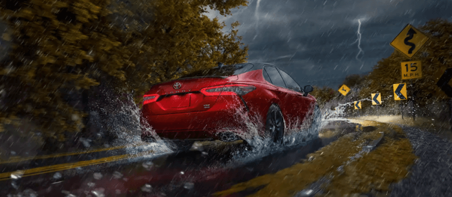 A rear shot of a 2024 Toyota Camry Hybrid midsize sedan model driving on wet roads in a thunderstorm