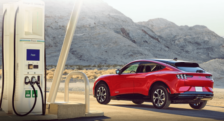 A 2023 Ford Mustang Mach-E all-electric compact SUV model parked near an EV charging station in the wild