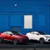 Red and white 2022 Toyota C-HR subcompact crossover SUV models parked in front of a blue painted brick wall