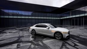 A white Genesis G90 full-size luxury sedan model parked on a asphalt lot streaked with water and tire marks