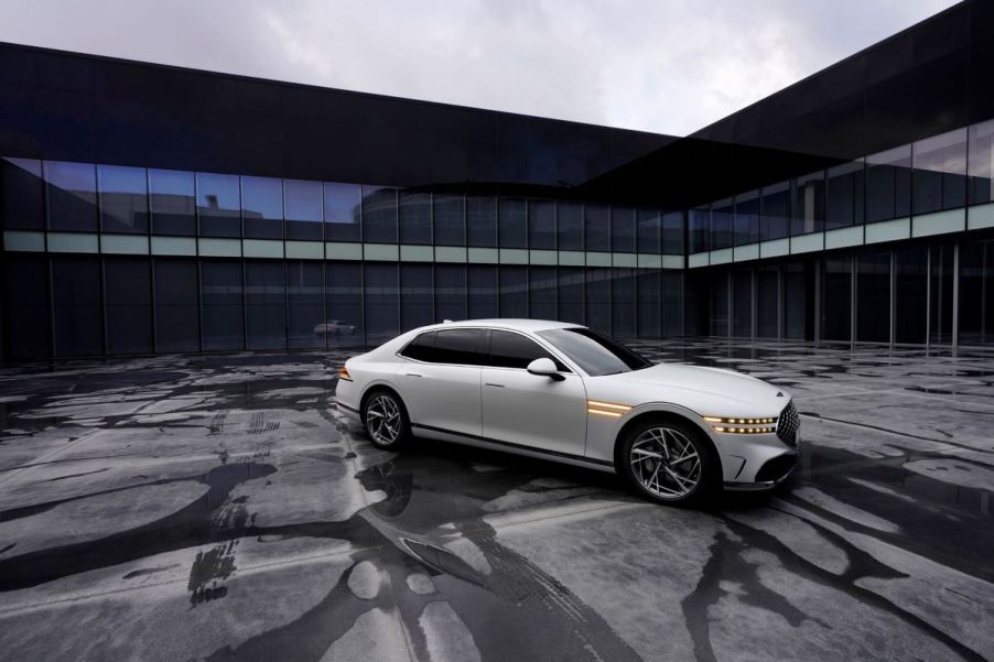 A white Genesis G90 full-size luxury sedan model parked on a asphalt lot streaked with water and tire marks