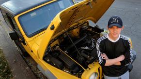 Matt Schilling with a yellow 2000 Jeep Wrangler with its hood popped for maintenance and surveying of auto parts