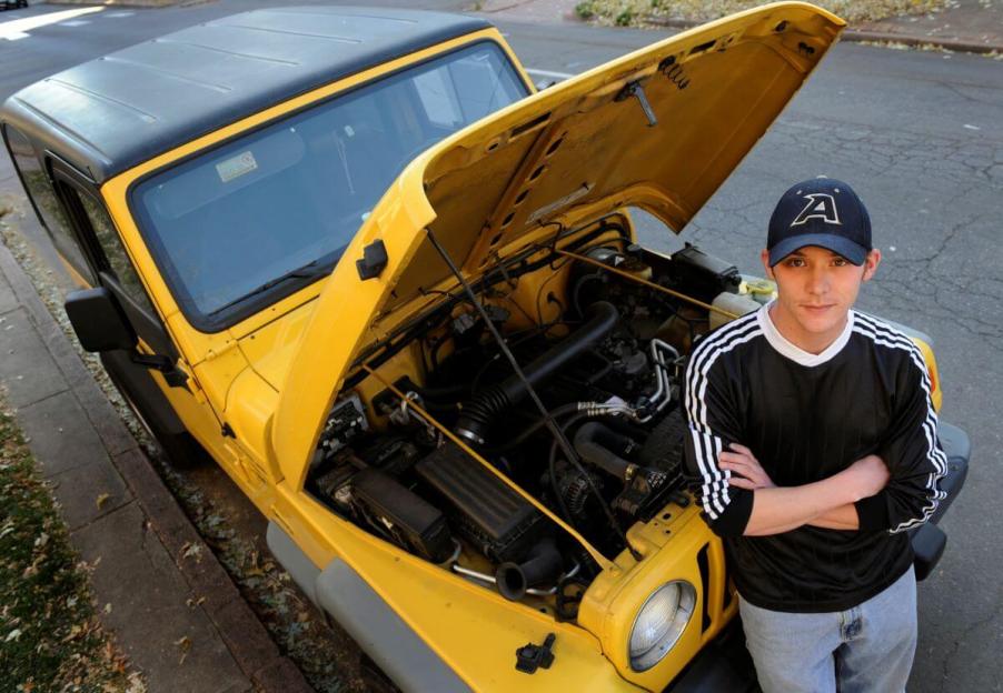 Matt Schilling with a yellow 2000 Jeep Wrangler with its hood popped for maintenance and surveying of auto parts