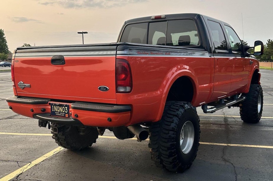 The tailgate of an orange 2004 Ford F-250 pickup truck parked in a parking lot, the sky visible in the background.