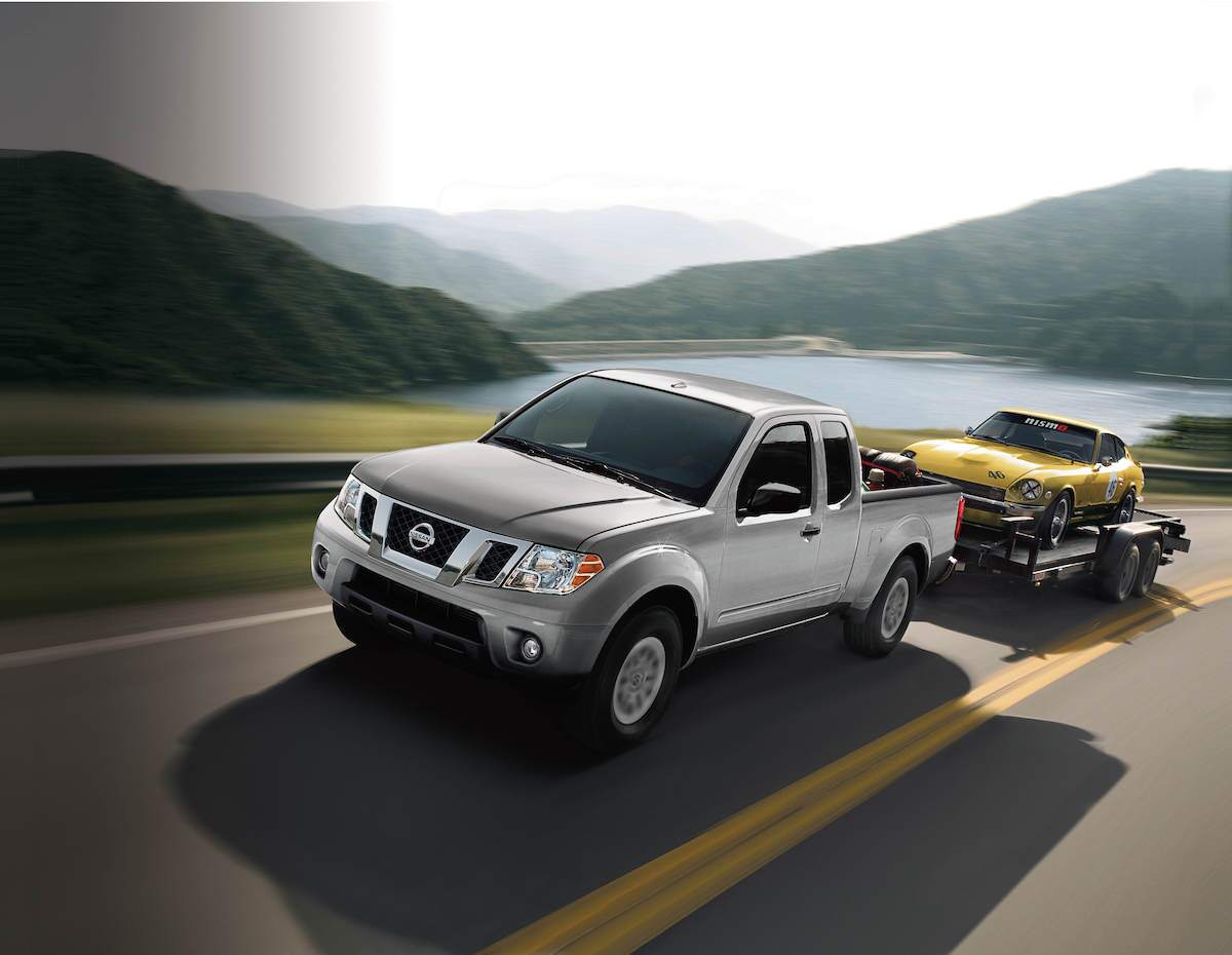 A silver 2018 Nissan Frontier towing a yellow classic Nissan sports car on a trailer