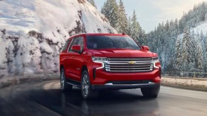 A red 2023 Chevrolet Suburban full-size SUV is driving on the road.